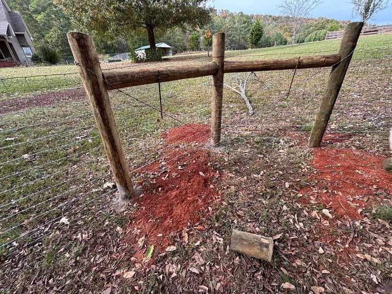 Wooden split-rail fence with red mulch around base posts in rural pasture