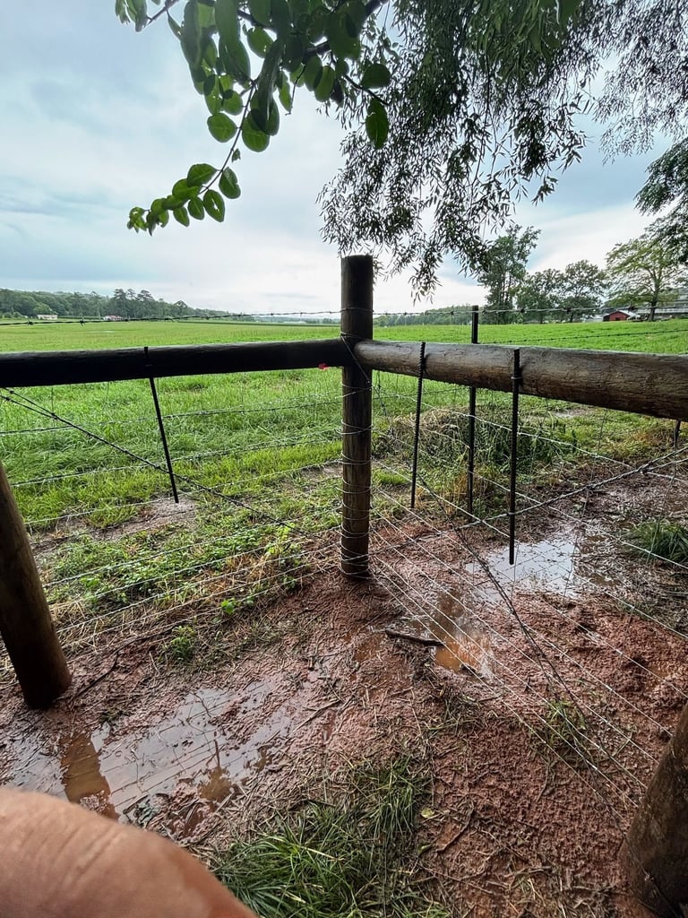 Rustic wooden fence with metal posts in muddy field overlooking green landscape