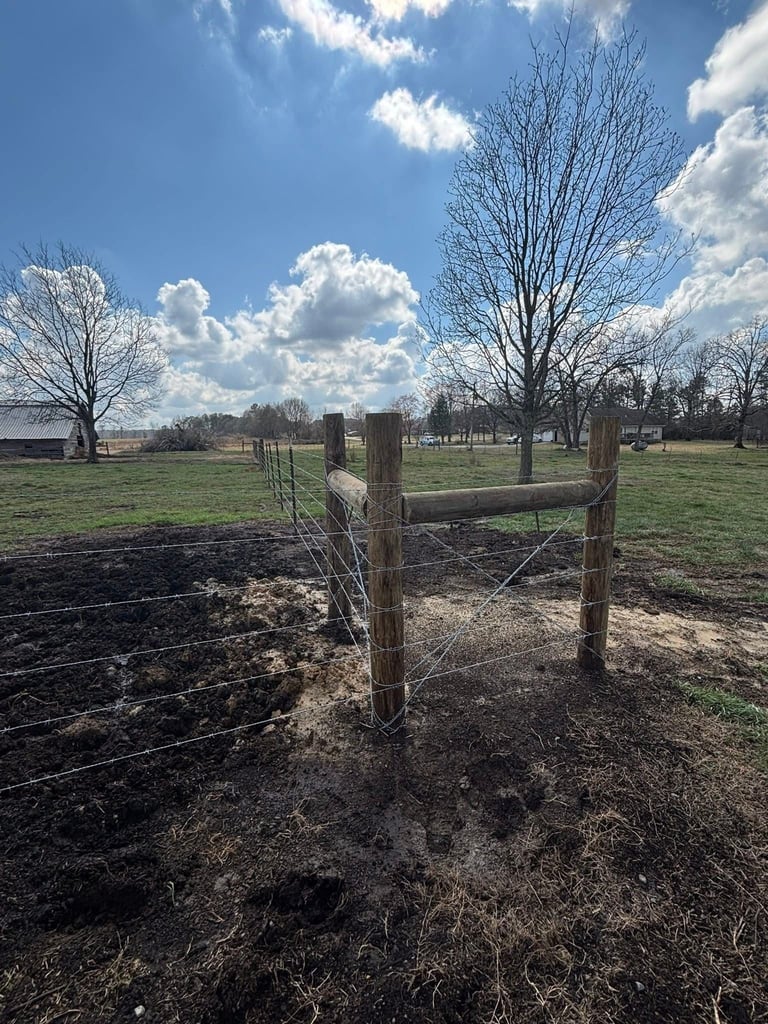 Wooden fence gate in a rural pasture with bare trees and blue sky with white clouds