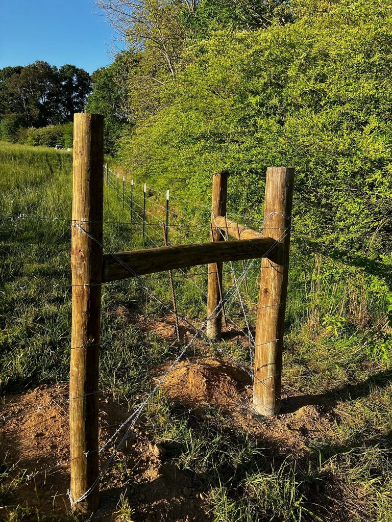 Wooden farm gate with metal cross-beam and wire fencing in grassy rural field